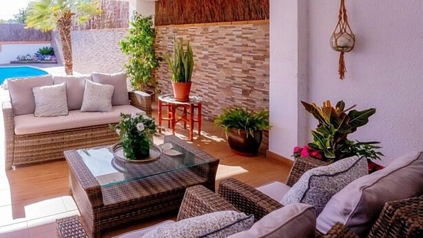 A sunlit living area with wicker furniture, a glass coffee table, and potted plants. - Stay U-nique Villa Marinada (Calafell)