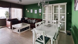 A modern living room with a dining area, green walls, a chandelier, and a large cabinet with glass doors. - Stay U-nique Villa Marinada (Calafell)