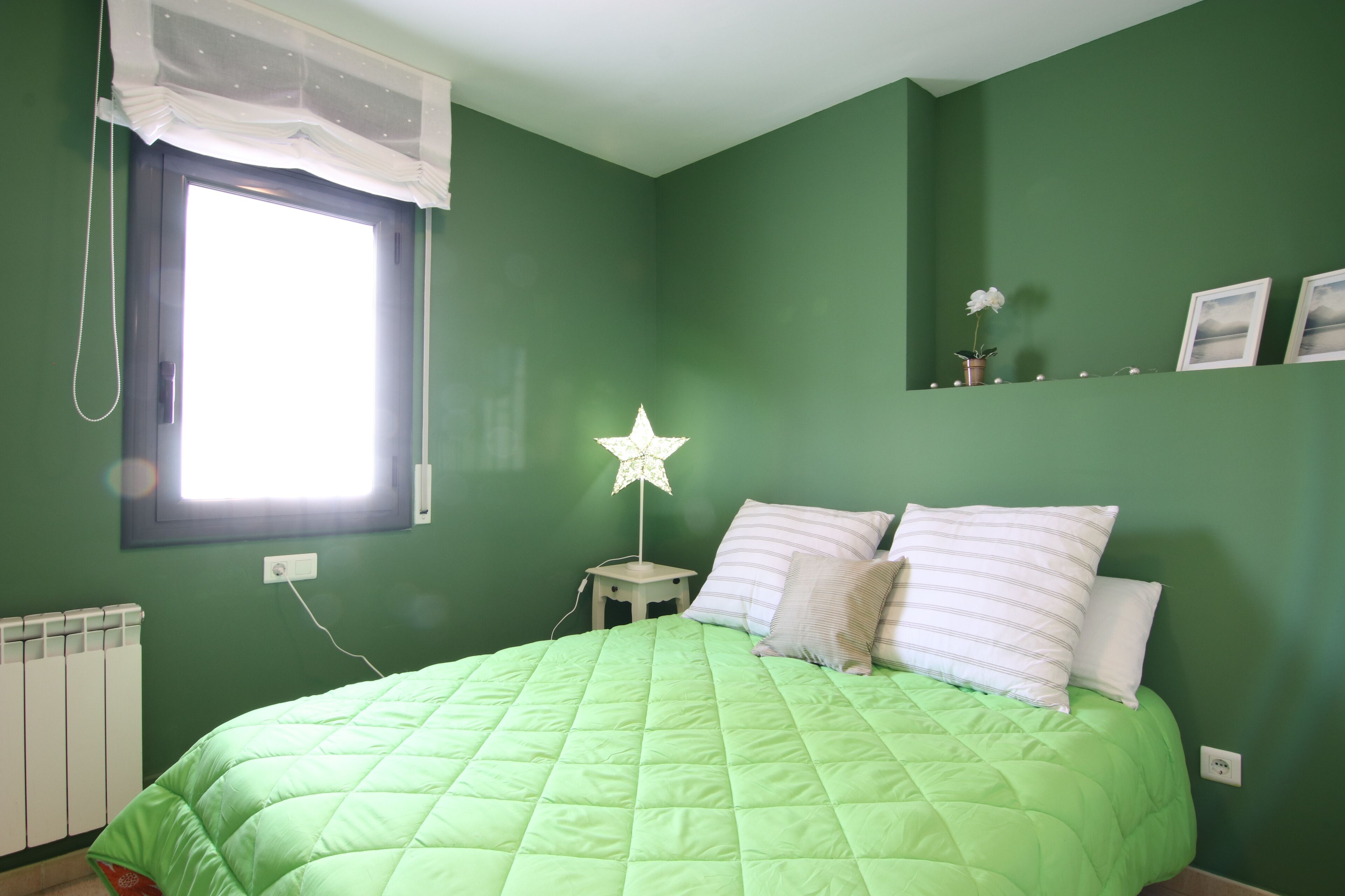 A room with a green wall, a bed with a green quilt, a star-shaped night light, and a window with a white valance.