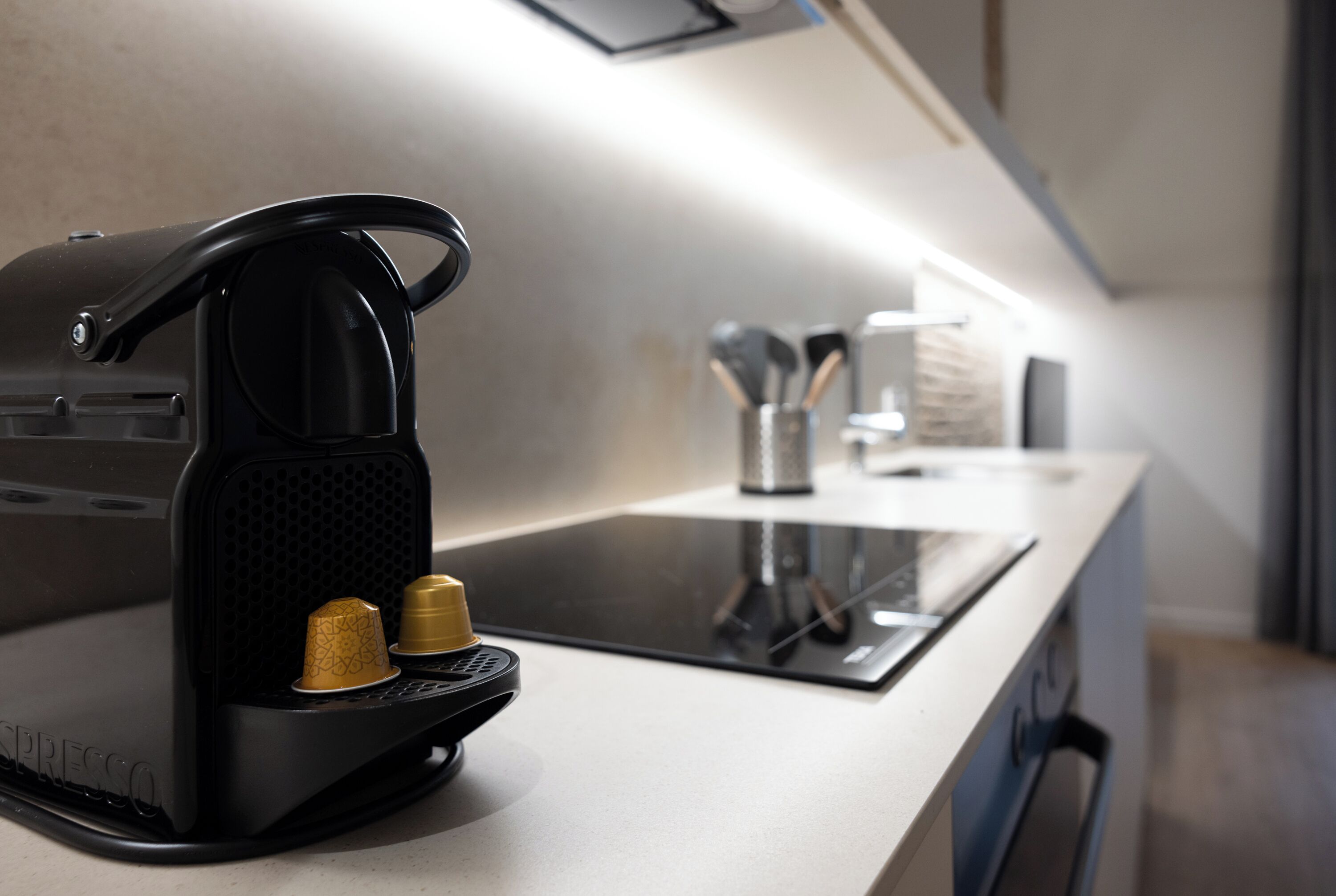A modern kitchen with a black espresso machine, a built-in induction cooktop, and a stainless steel utensil holder.