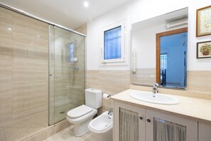 Ein modernes Badezimmer mit einer Duschkabine, einer Toilette, einem Bidet und einem Waschbecken mit Spiegel darüber.