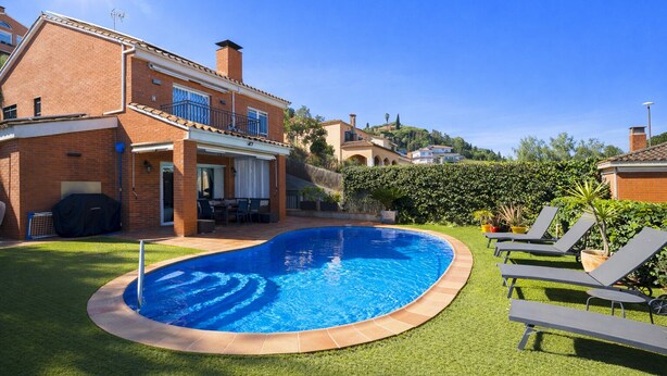 Une piscine entourée d’une pelouse bien entretenue, une terrasse avec des meubles d’extérieur et une maison en briques dotée d’un balcon.