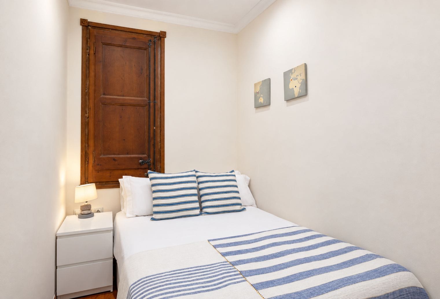 A bedroom with a bed, a nightstand, a wooden door, and two wall-mounted maps.