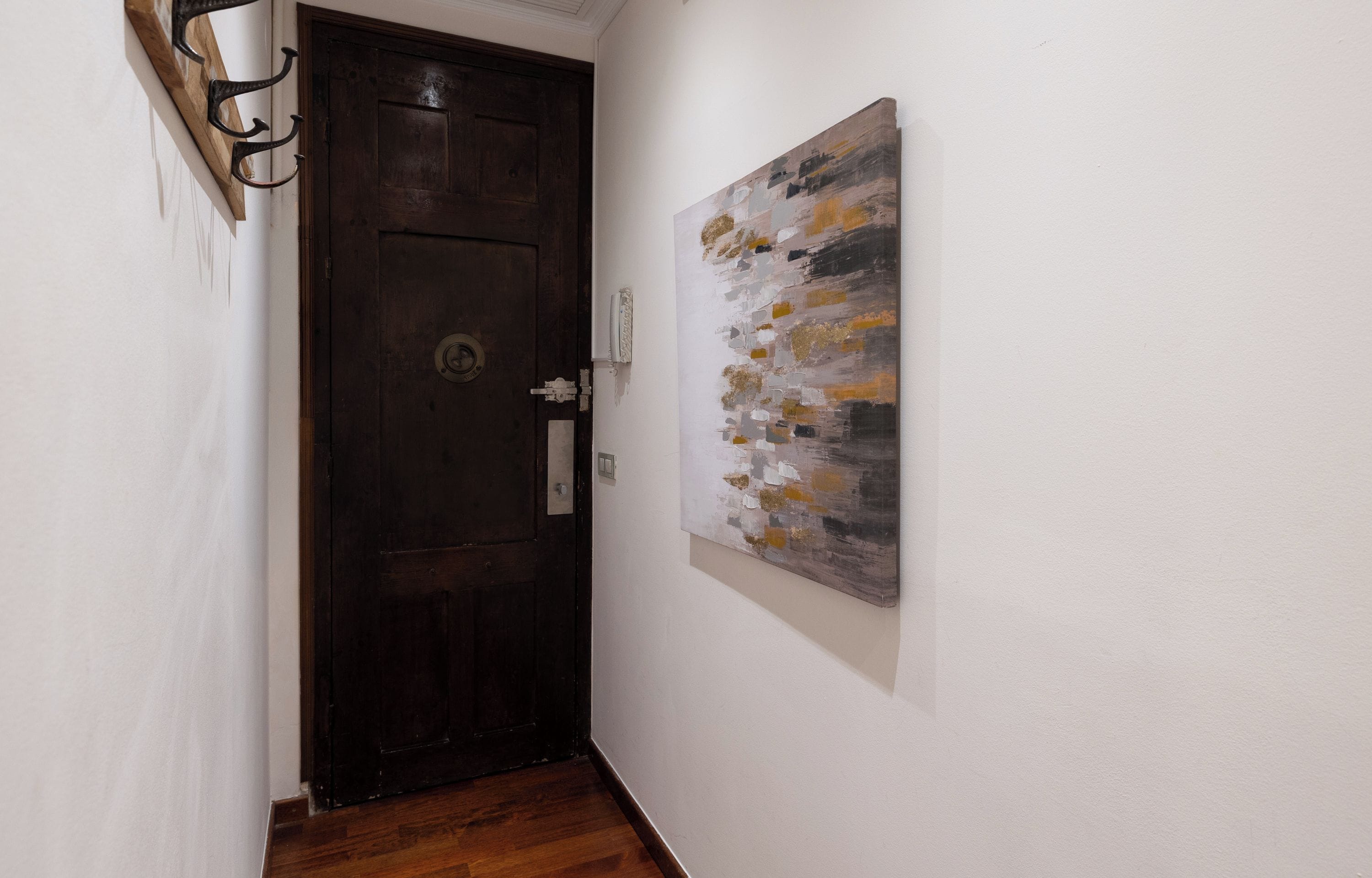 A hallway with a wooden door and a wall-mounted abstract painting.