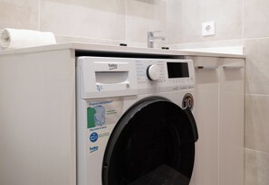 Vista frontal de una lavadora moderna y compacta, con panel de control digital, puerta de carga frontal y un pequeño panel superior.
