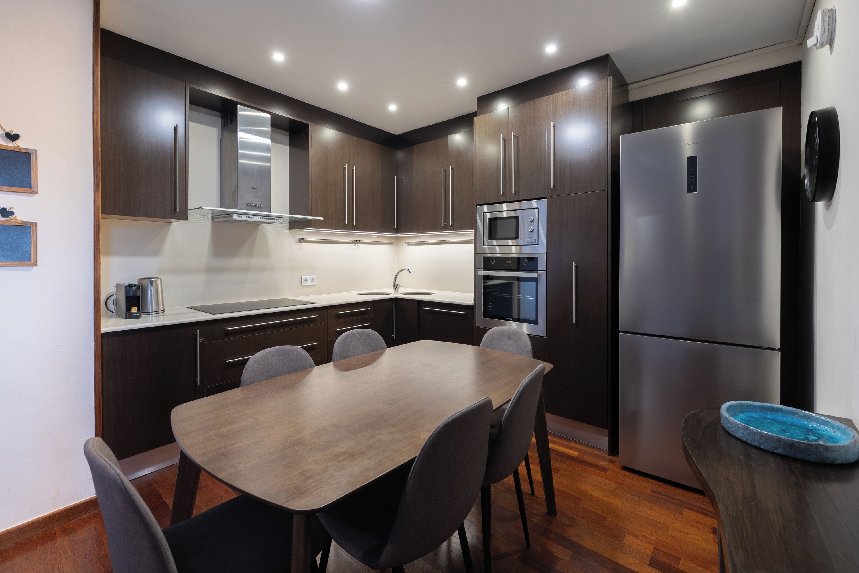 A modern kitchen with dark wood cabinets, stainless steel appliances, and a dining table with chairs.