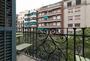 Een balkon met een sierhek van smeedijzer, een bankje en uitzicht op meerverdieping woongebouwen.