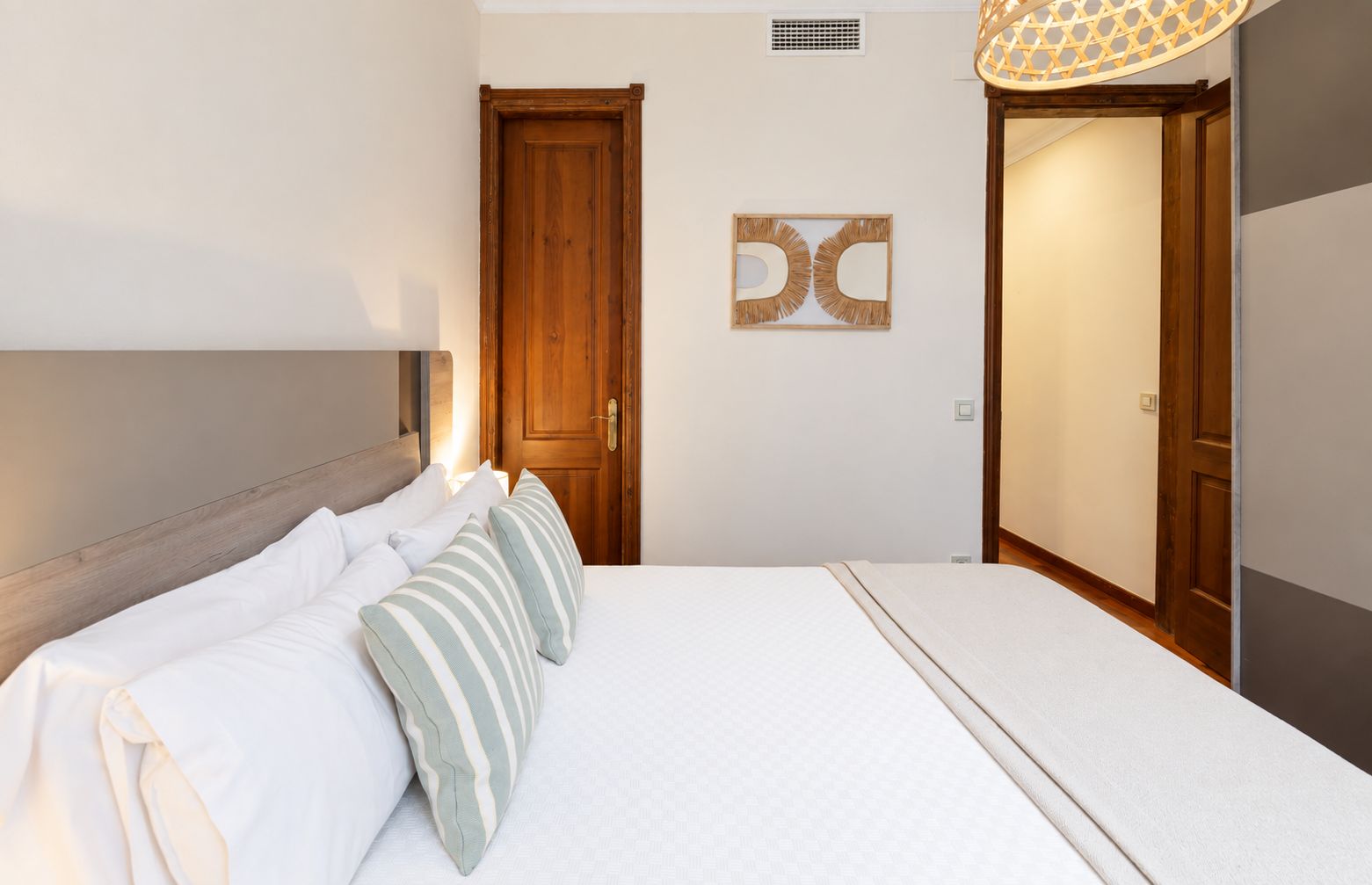 A bedroom with a bed, pillows, a wooden door, and a wall-mounted light fixture.