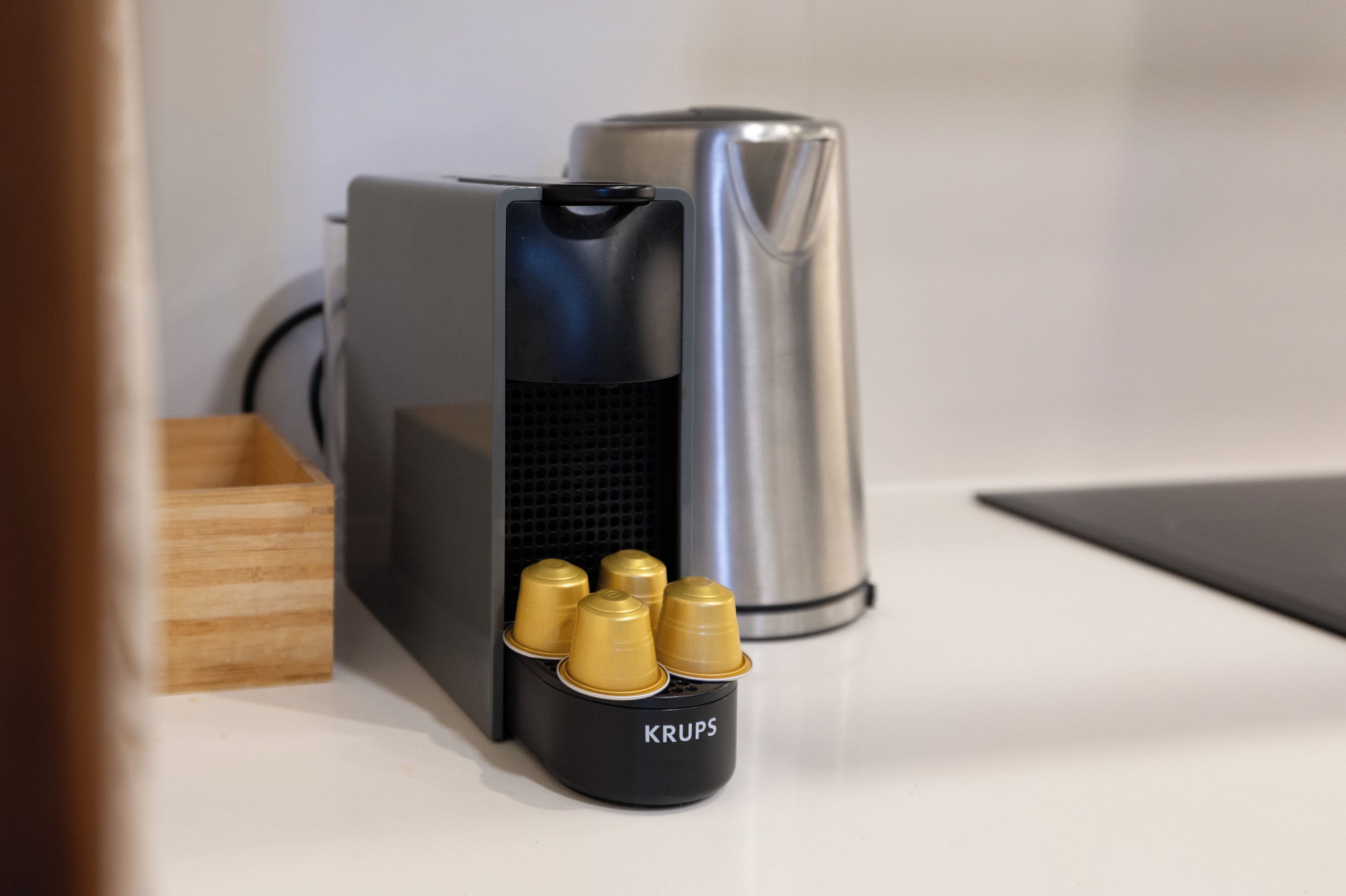 A black electronic device with a cylindrical metallic object beside it, and a black container labeled 'KRUPS' with several gold-colored objects.