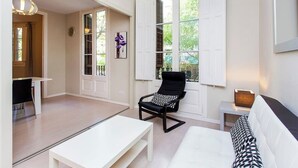 Ein modernes Wohnzimmer mit einem weißen Sofa, einem schwarz-weißen Ohrensessel, einem weißen Couchtisch und einem Essbereich mit weißem Tisch und schwarzen Stühlen.