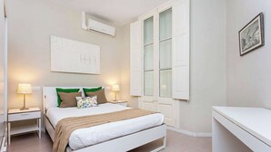 Ein modernes Schlafzimmer mit Bett, Nachttischen, einem Schreibtisch und einem Fenster mit Rollläden.