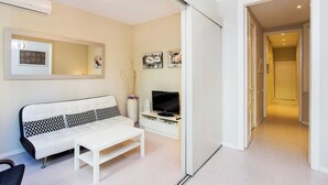 Ein modernes Wohnzimmer mit einem weißen Sofa, einem Couchtisch, einem Flachbildfernseher und einer Schiebetür zu einem Flur.