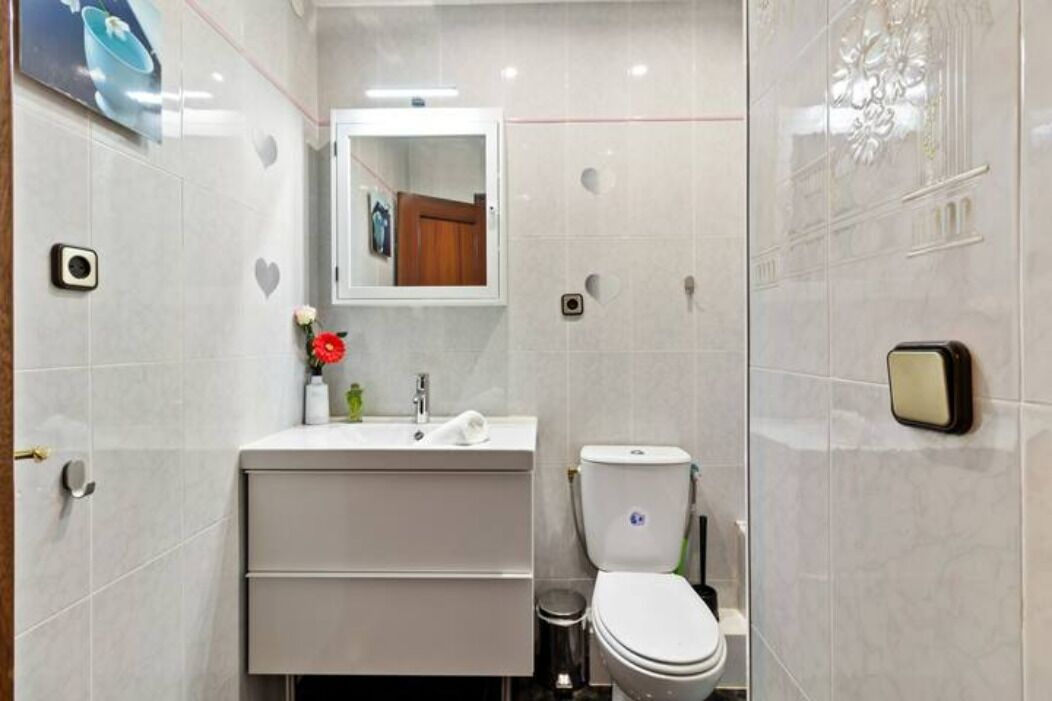 Un baño moderno con lavamanos, espejo e inodoro blancos.
