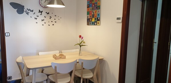 A dining area with a wooden table, white chairs, a vase with flowers, butterfly wall decals, and a colorful abstract art piece. - Stay U-nique Apartments La Bordeta (Barcelona)