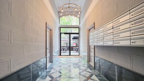 A hallway with a patterned floor, a row of mailboxes on one side, and a door leading to an outdoor area.