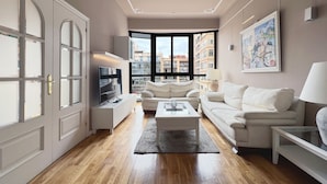 A modern living room with a large window, a flat-screen TV, a sofa, a coffee table, and a painting on the wall.