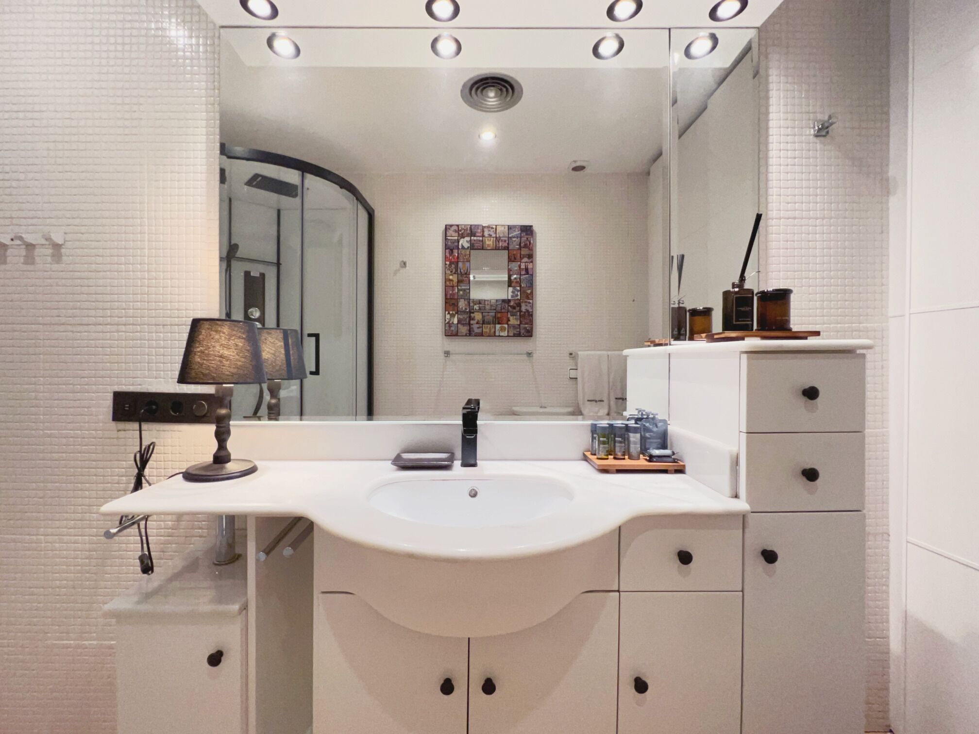 A modern bathroom with a white sink, a mirror, and a shower area.