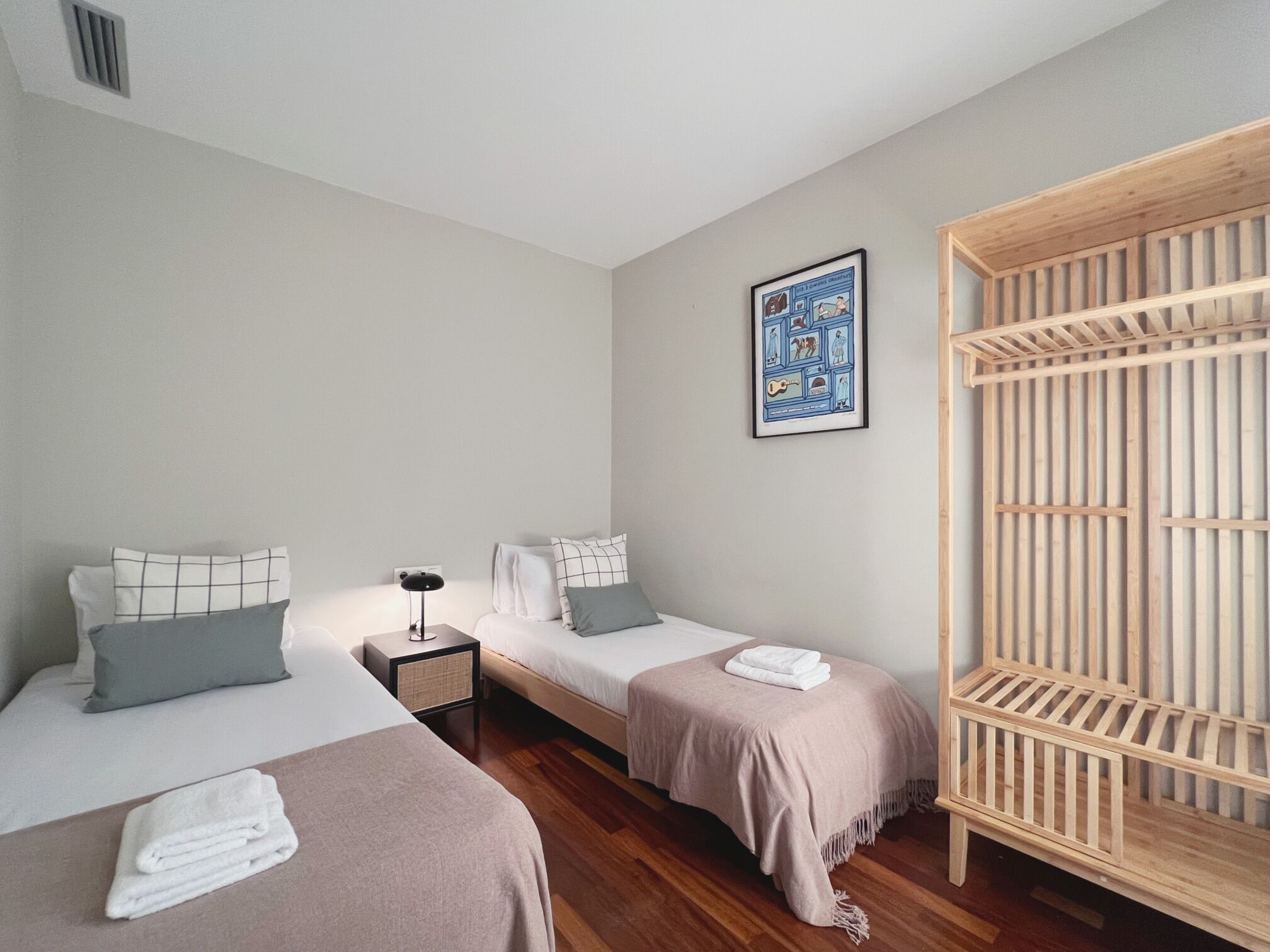 A bedroom with two beds, a nightstand, a lamp, a wooden crib, and a framed picture on the wall.