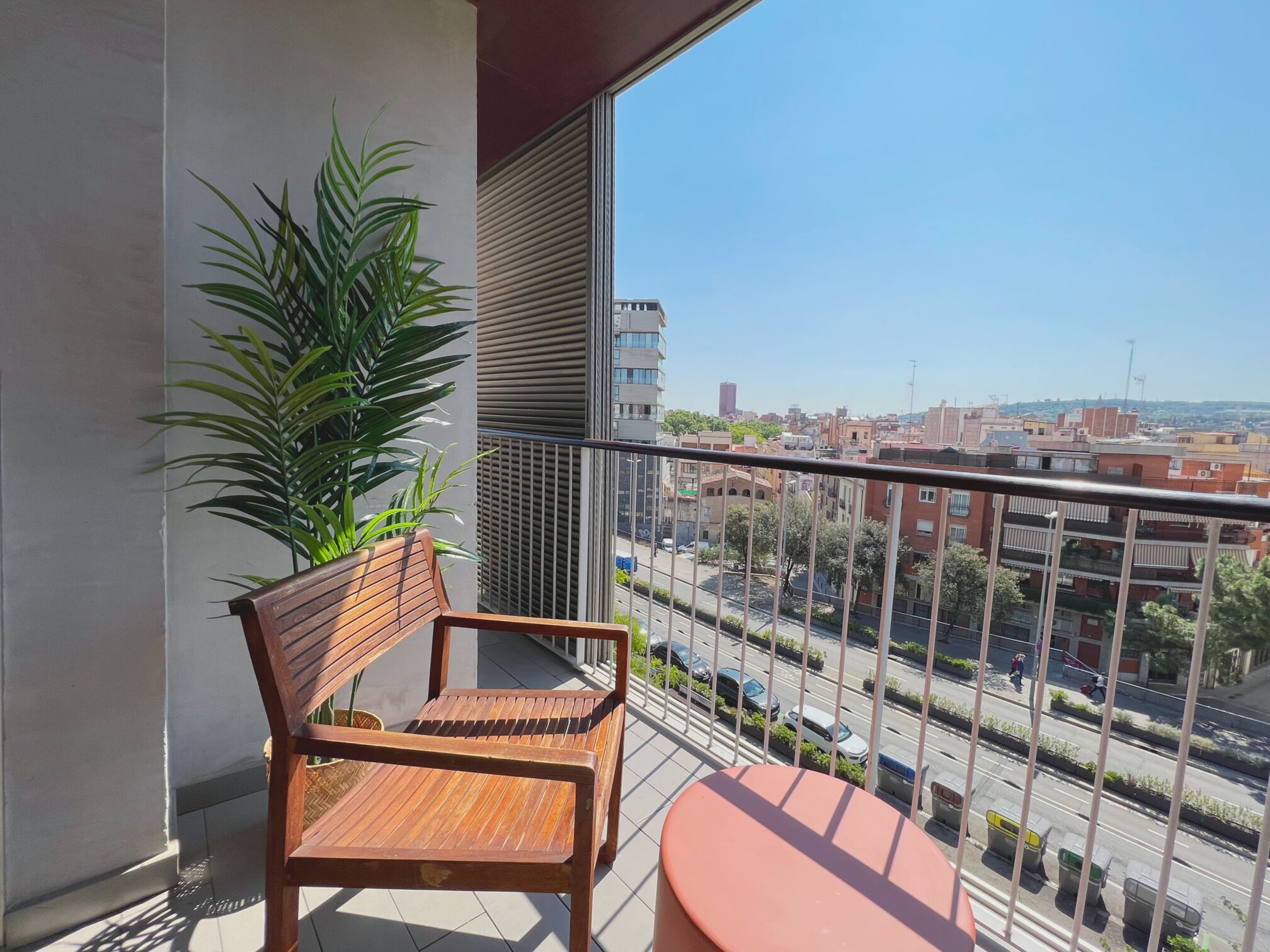 A balcony with a wooden chair and a small round table, a potted plant, and a city view.