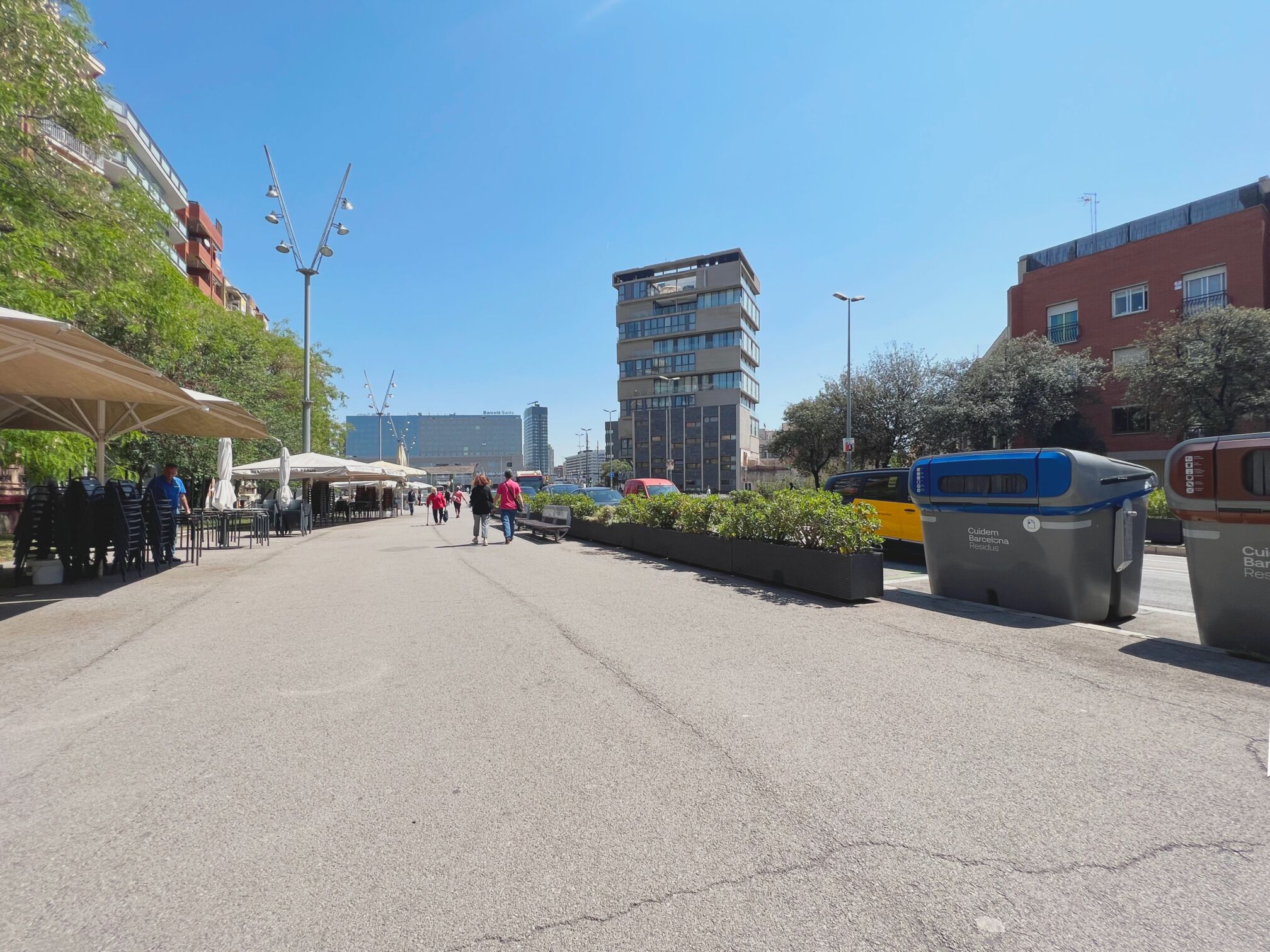 Una calle con mesas al aire libre, una parada de autobús y edificios al fondo.