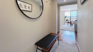A hallway with a round mirror, a framed picture, a bench, and a view of an outdoor balcony with a table and chairs. - Stay U-nique Apartments Sants II (Barcelona)
