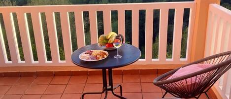 A balcony with a round table, two wicker chairs, and a potted plant.