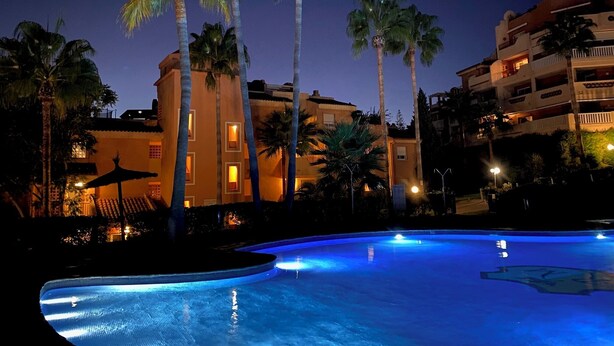 A swimming pool with palm trees and a building with illuminated windows at night. - Stay U-nique Apartments Benajarafe (Marbella)
