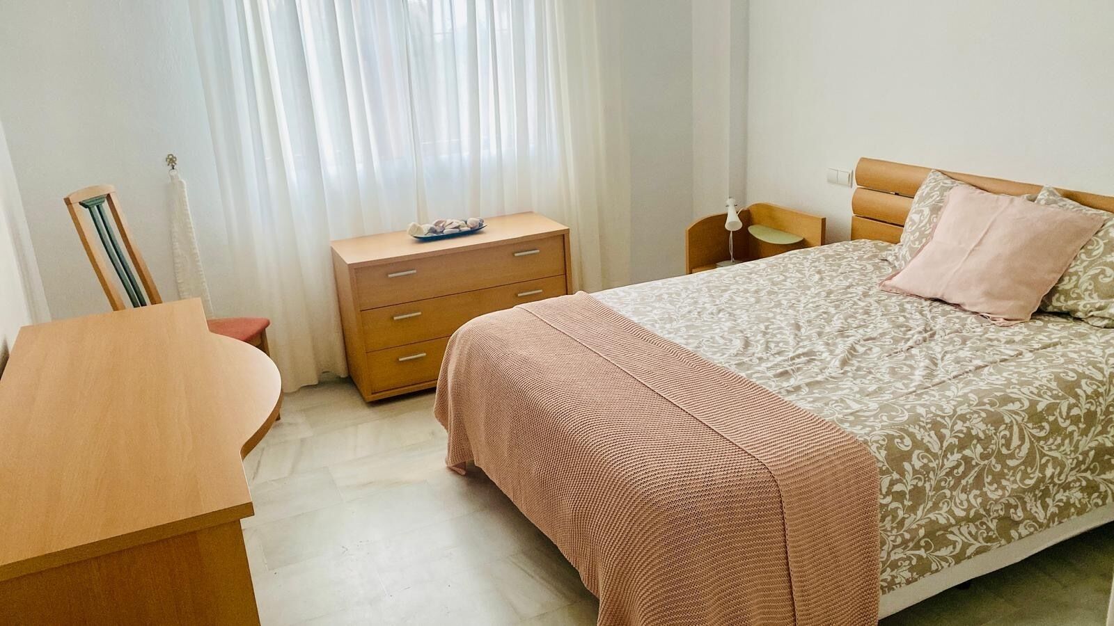A bedroom with a bed, a wooden nightstand, a dresser, and a desk.