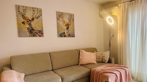A living room with a beige sofa, two paintings of deer, a floor lamp, and a pink blanket. - Stay U-nique Apartments Benajarafe (Marbella)