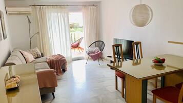 Una sala de estar moderna con un sofá, una mesa de comedor con sillas, un televisor y un balcón con una silla.