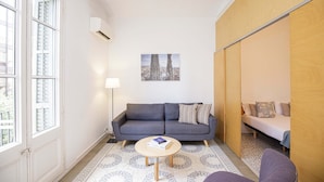 Ein gemütlicher Wohnbereich mit grauem Sofa, rundem Couchtisch, Bett mit Holz Kopfteil und Wandgerät zur Klimatisierung.