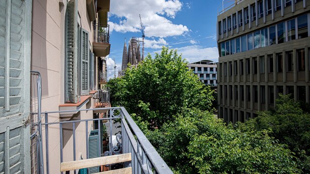Blick auf ein Gebäude mit einem Balkon, der auf eine von Bäumen gesäumte Straße und einen Baukran im Hintergrund blickt.