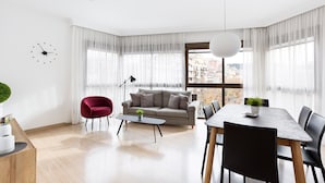 Un salon moderne avec un canapé, un fauteuil rouge, une table à manger avec des chaises et une grande fenêtre donnant sur la ville.