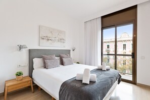 A modern bedroom with a large bed, a view of the city through a large window, and a small bedside table with a plant. - Stay U-nique Apartments Sant Antoni II (Barcelona)