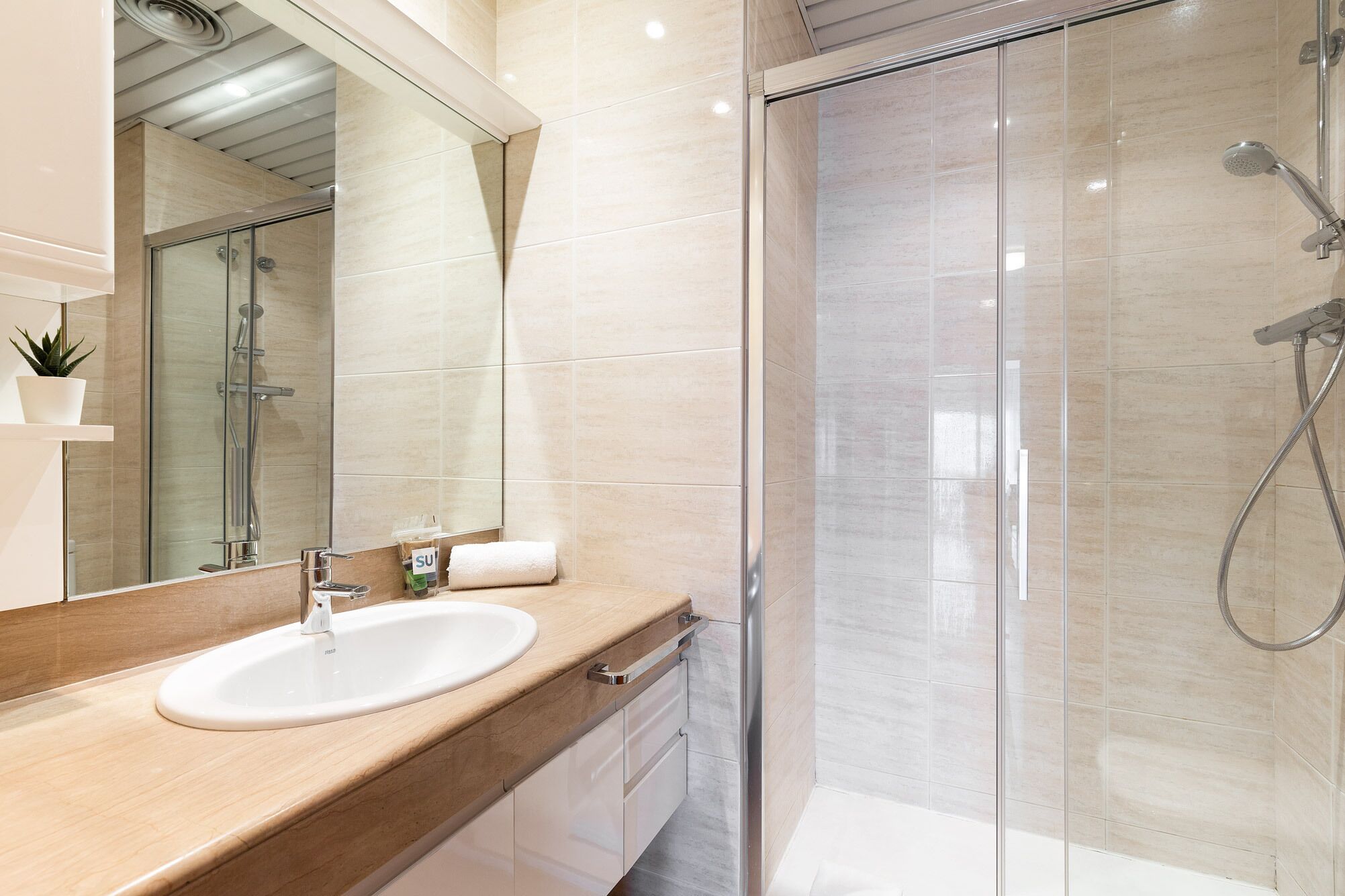 Un baño moderno con cabina de ducha de vidrio, un lavabo blanco y un espejo grande.
