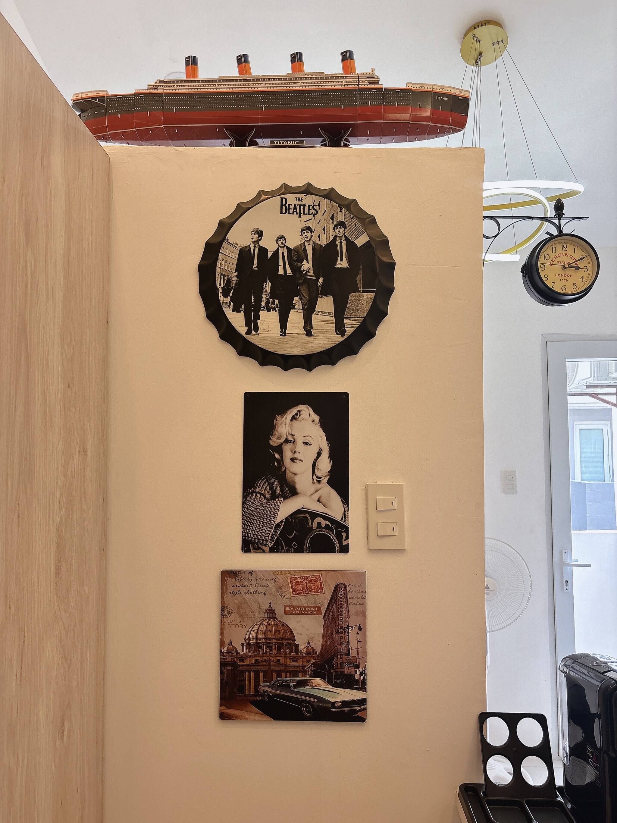 A wall with a clock, a framed Beatles photo, a framed Marilyn Monroe photo, and a framed cityscape photo.