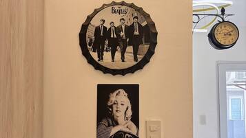 A wall with a clock, a framed Beatles photo, a framed Marilyn Monroe photo, and a framed cityscape photo.