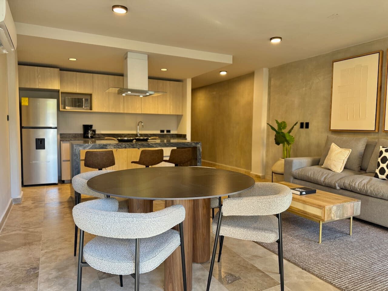 A modern kitchen with a central island, a dining area with a round table and chairs, and a living area with a sofa and a coffee table.