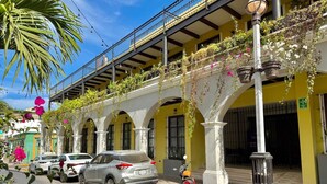 Vista callejera con coches estacionados y una motocicleta, un edificio con paredes y arcos amarillos, y un farol.
