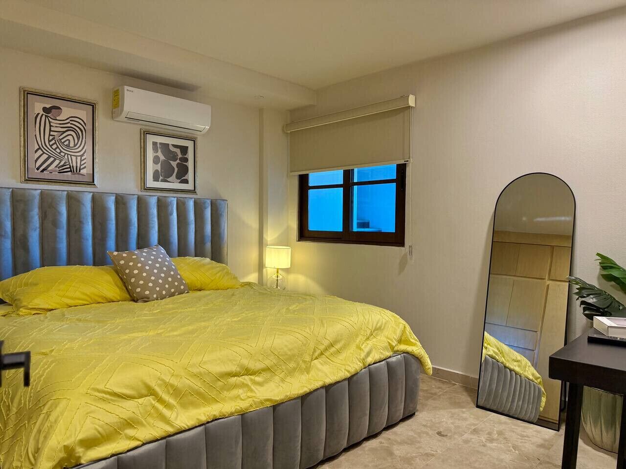 A bedroom with a bed, a bedside table, a mirror, and artwork on the wall.