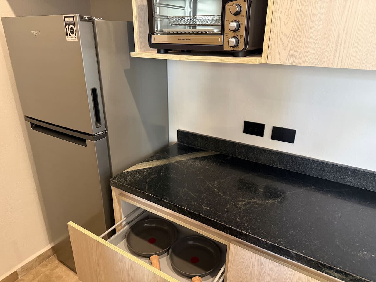 A compact kitchen with a built-in microwave, a stainless steel refrigerator, and a black countertop.