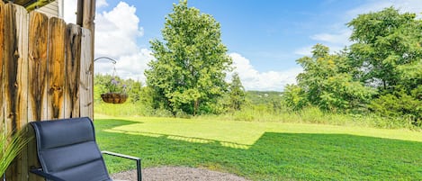 A patio with a black chair and table, a wooden fence, and a view of a grassy area with trees.