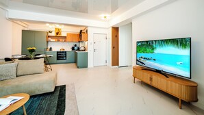 Un soggiorno moderno con una TV a schermo piatto, un divano e un'area pranzo con cucina sullo sfondo.