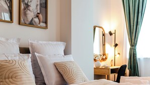 Un letto rifatto con lenzuola bianche e beige, un comodino con una lampada e uno specchio sulla parete.