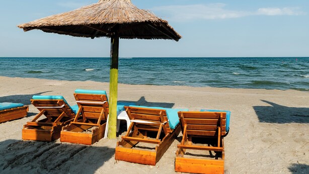 Una spiaggia con lettini di legno e un ombrellone di paglia.