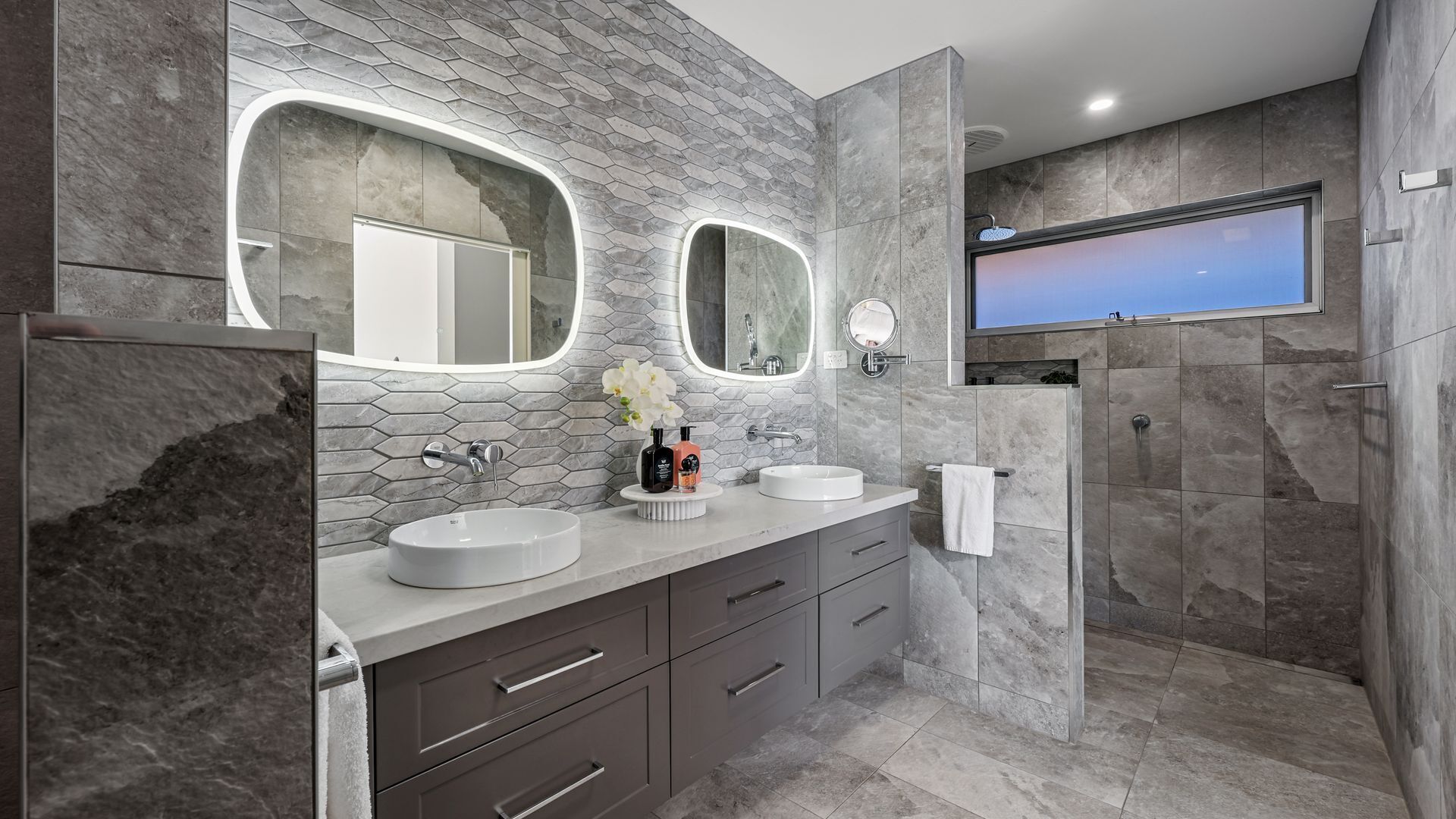 A modern bathroom with two sinks, a large mirror, and a shower area.