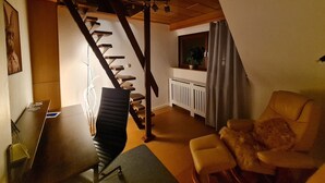 A modern living room with a staircase, a comfortable chair, a radiator, and a window with a curtain.