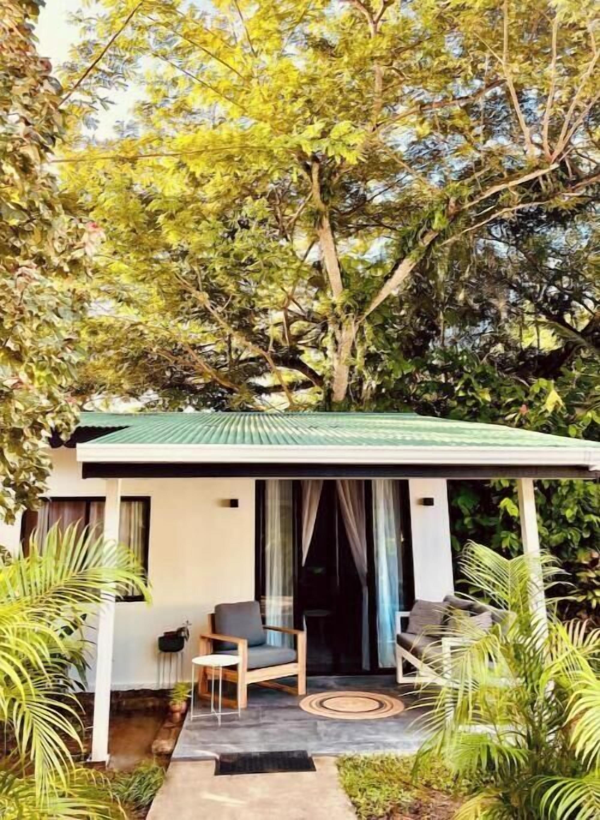 A small, modern house with a green roof, a covered porch, and a seating area with a table and chairs.