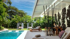 A poolside area with a lounge chair, a small table, and a pergola. - La Prometida - House Marea (Puerto Viejo)