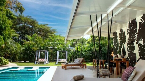 A poolside area with a covered seating area, a swing chair, and a dining table with chairs.